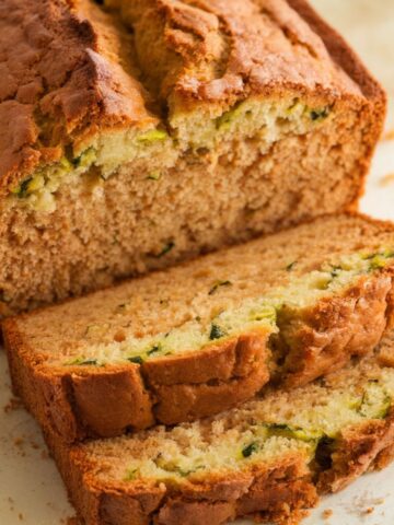 Homemade gluten-free zucchini bread with a golden crust, moist crumb, and visible flecks of zucchini, sliced thick for a rustic.