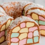 Colorful sliced lolly cake with pastel marshmallow pieces embedded in a golden-brown biscuit base, coated in shredded coconut