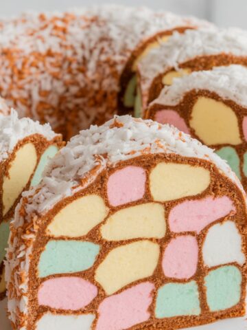 Colorful sliced lolly cake with pastel marshmallow pieces embedded in a golden-brown biscuit base, coated in shredded coconut