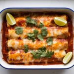 Baked Boulders Enchilada Recipe in a white dish with red sauce, melted cheese, and fresh garnishes on a clean kitchen counter