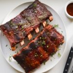 Perfectly cooked beef back ribs with a rich mahogany bark, glazed and sprinkled with herbs, served on a white plate.