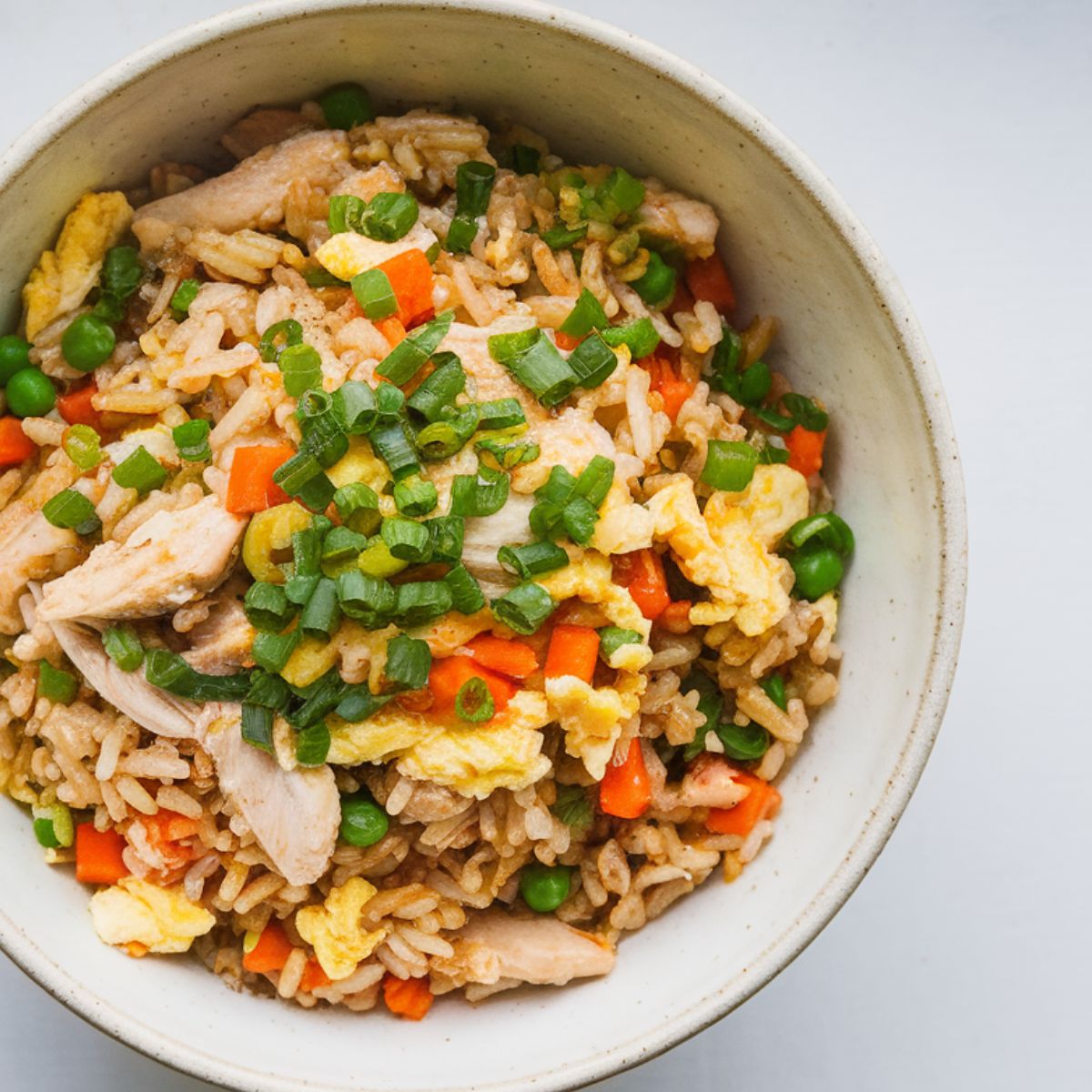 Benihana-style chicken fried rice served in a white ceramic bowl with green onion garnish, placed on a clean white counter.