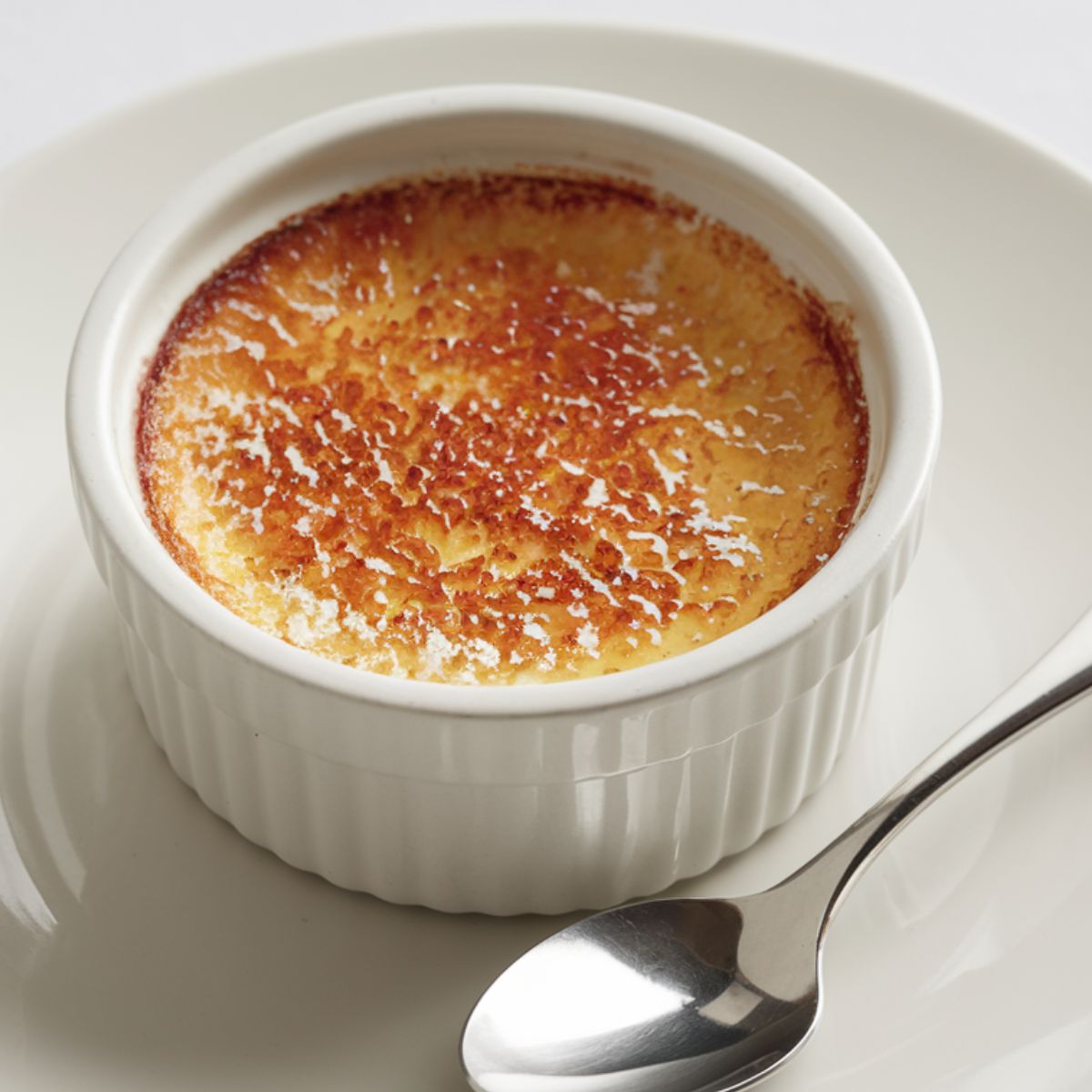 Homemade crab brulee served on a ramekin on a white plate.