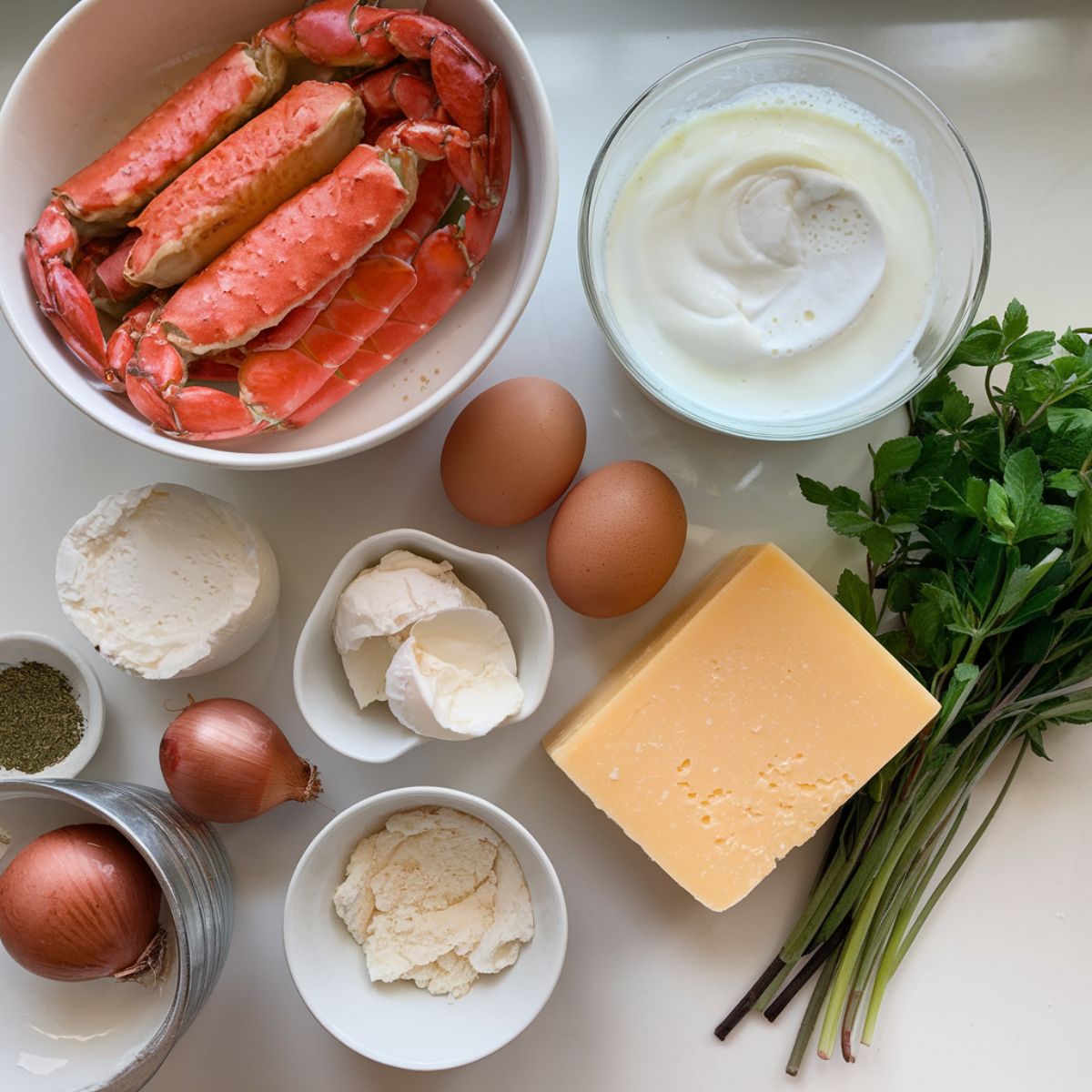 crab brulee ingredients include fresh lump crab meat, heavy cream, eggs, aged Gruyere cheese, shallots, fresh herbs, and white wine laid out on a white kitchen counter.