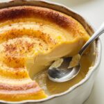 Close-up of creamy Amish baked custard with a golden top, a spoon revealing its silky texture.