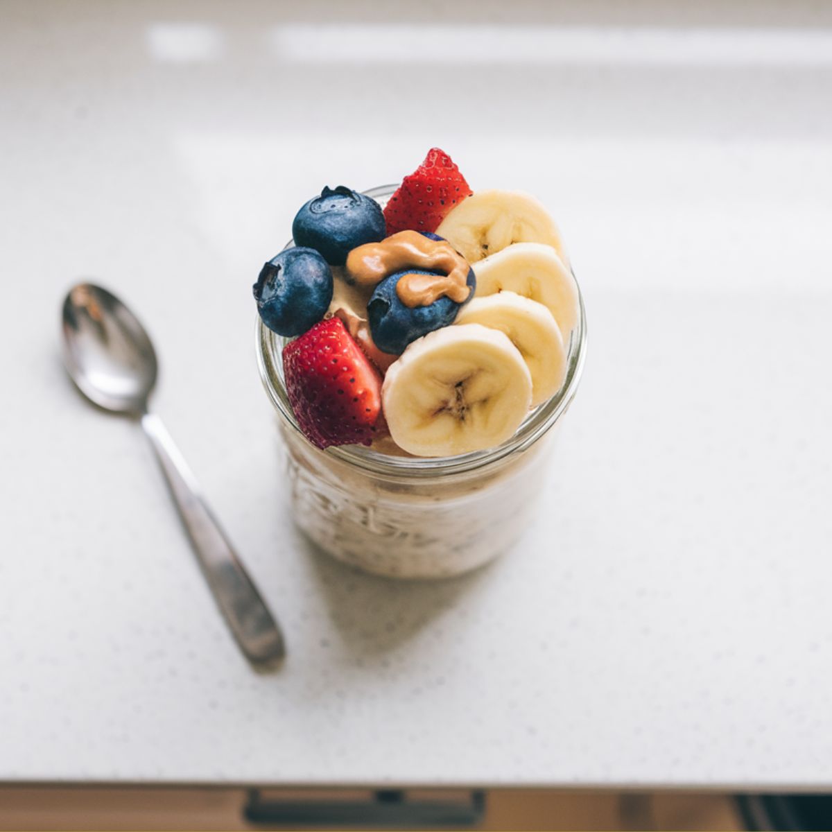 Completed protein overnight oats in a jar topped with berries, bananas, and peanut butter