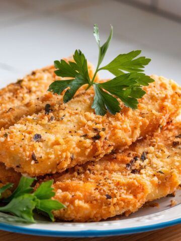 Golden fried fish with a crispy coating, garnished with parsley, served on a white plate.