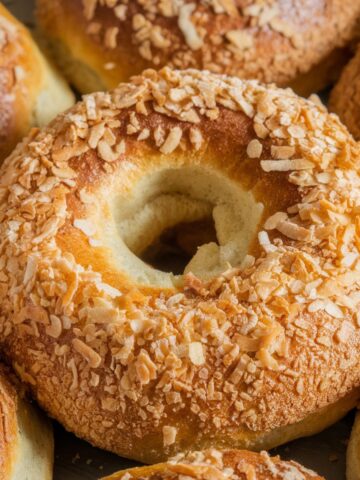 A homemade sourdough bagel with a golden-brown crust, generously coated with toasted coconut flakes, giving it a crisp, textured finish