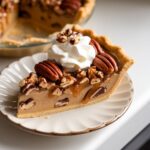 A slice of homemade pecan cream pie with a creamy custard layer, toasted pecans, and a dollop of whipped cream on a white plate.