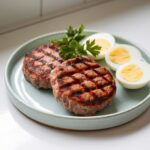 Grilled turkey breakfast sausage patties served with hard-boiled eggs and fresh parsley on a ceramic plate."