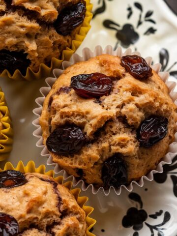 Raisin bran muffins resting on a decorative white plate with a black floral pattern.