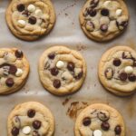 Six freshly baked Mama Kelce chocolate chip cookies on parchment paper, golden brown with slightly crispy edges and melted chocolate chips, arranged naturally with a homemade look.