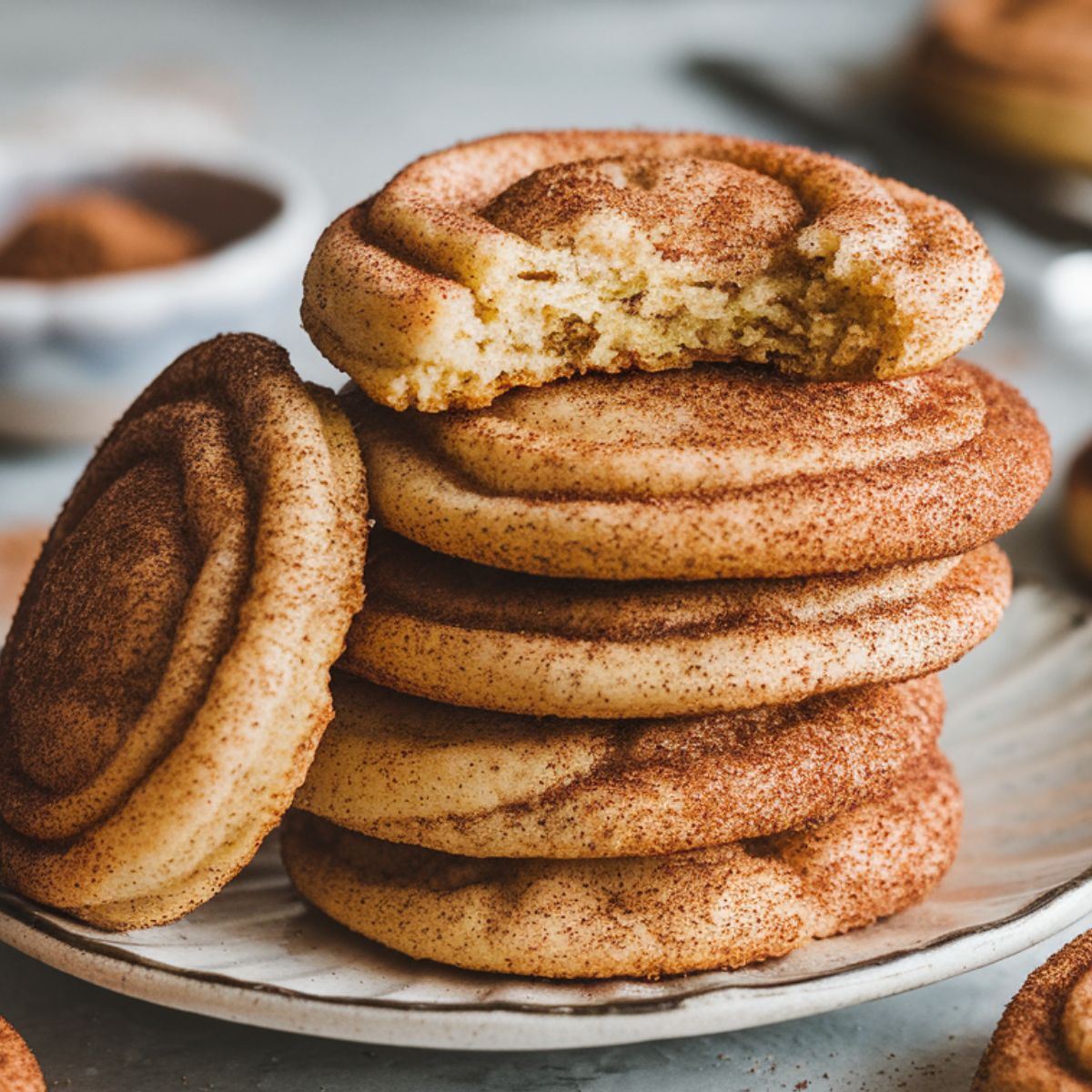 A stack of golden-brown snickerdoodle cookies with cinnamon-sugar coating on a white plate, placed on a home kitchen counter.