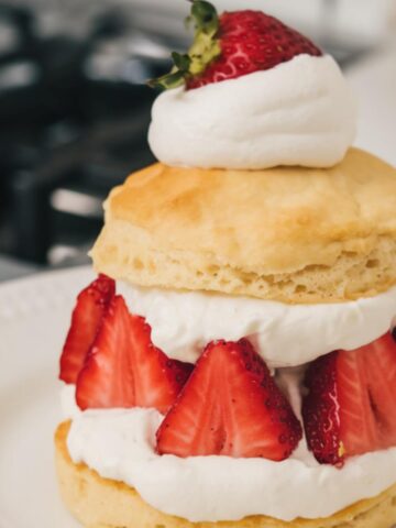 Rustic homemade Bisquick strawberry shortcake with flaky, uneven biscuit, fresh strawberries, and dollops of whipped cream on a white plate.