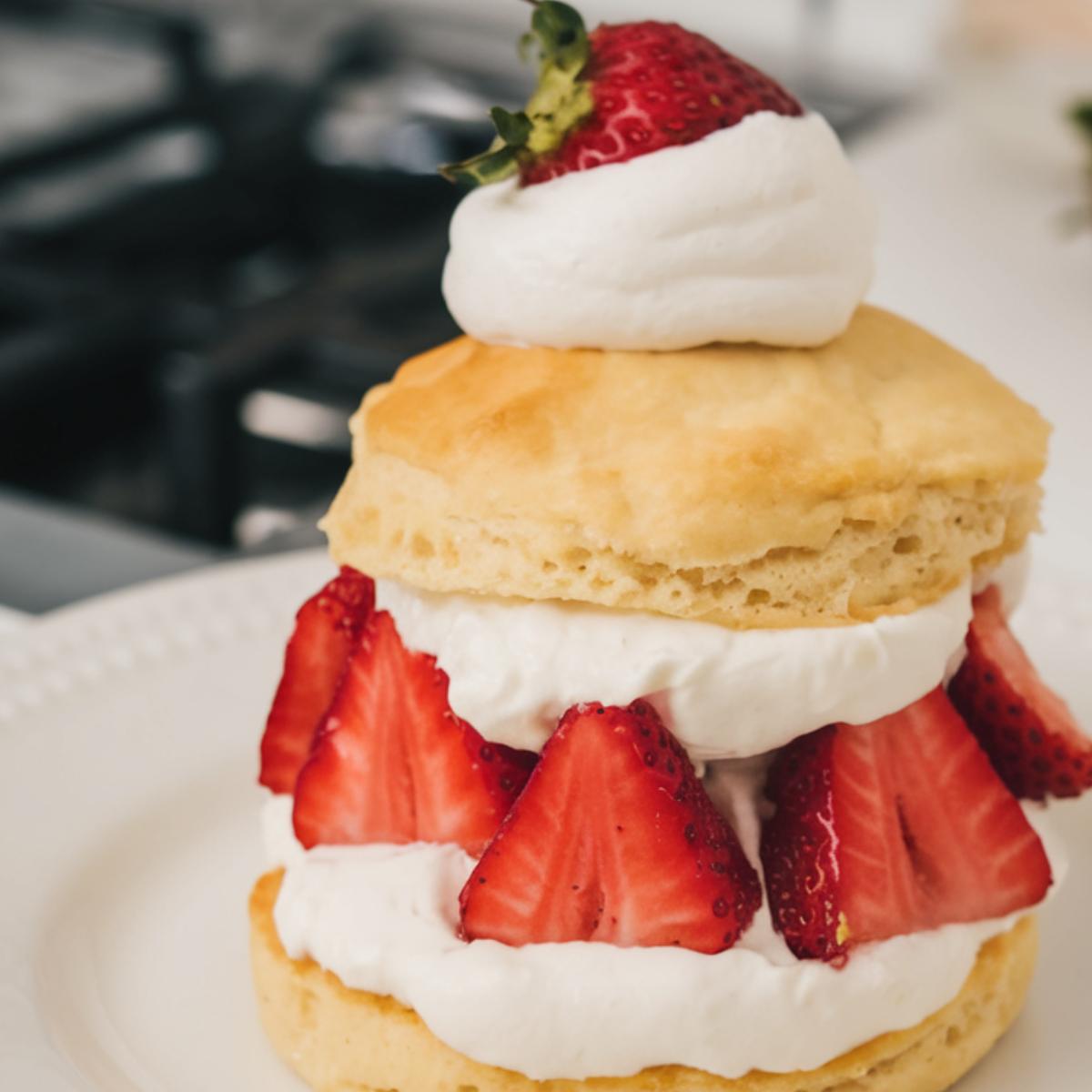 Rustic homemade Bisquick strawberry shortcake with flaky, uneven biscuit, fresh strawberries, and dollops of whipped cream on a white plate.