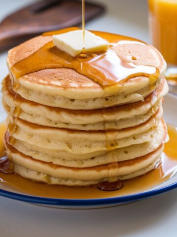 A stack of fluffy, golden pancakes drizzled with maple syrup and butter, served on a white plate. Perfect homemade Cracker Barrel-style pancakes on a kitchen counter.