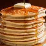 A stack of five thick, fluffy homemade hotcakes with slightly uneven edges, topped with melting butter and drizzled with maple syrup, creating a warm and inviting look.