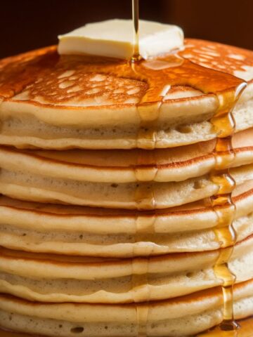 A stack of five thick, fluffy homemade hotcakes with slightly uneven edges, topped with melting butter and drizzled with maple syrup, creating a warm and inviting look.