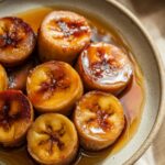 Homemade caramelized fried bananas with golden-brown crispy edges, coated in glossy syrup, served on a ceramic plate with a warm, natural look.