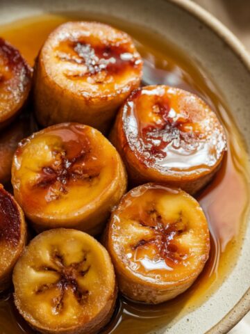 Homemade caramelized fried bananas with golden-brown crispy edges, coated in glossy syrup, served on a ceramic plate with a warm, natural look.