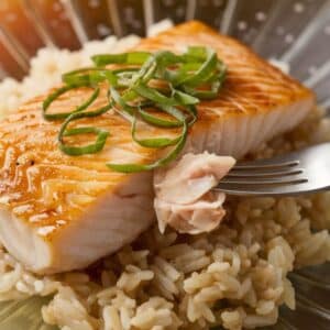 A homemade miso-glazed sablefish fillet, slightly caramelized with a glossy finish, garnished with sesame seeds and green onions, served on a rustic ceramic plate.