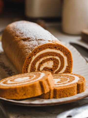 Homemade Libby’s pumpkin roll sliced on a plate, showing a creamy swirl filling with powdered sugar dusted on top