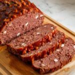 Homemade meatloaf with a glossy glaze, sliced to reveal a moist, seasoned interior on a white kitchen counter.