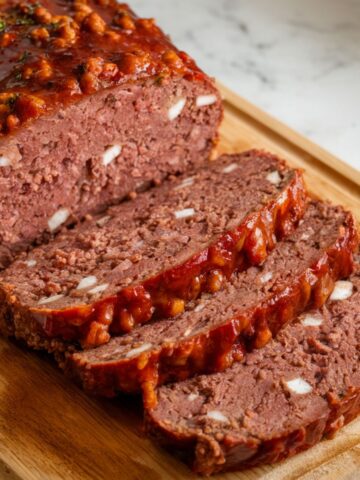 Homemade meatloaf with a glossy glaze, sliced to reveal a moist, seasoned interior on a white kitchen counter.