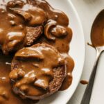 old fashioned salisbury steak with mushroom-onion gravy, mashed potatoes, and green beans on a white kitchen counter, taken from an overhead angle.