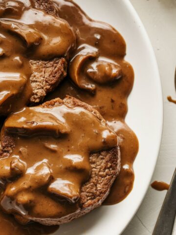 old fashioned salisbury steak with mushroom-onion gravy, mashed potatoes, and green beans on a white kitchen counter, taken from an overhead angle.