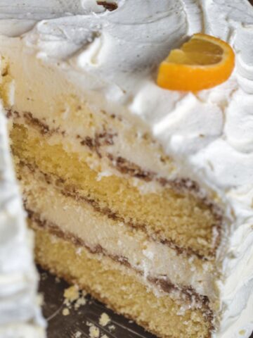 A homemade Pig Pickin Cake with fluffy whipped frosting and moist yellow cake layers, garnished with mandarin orange slices.