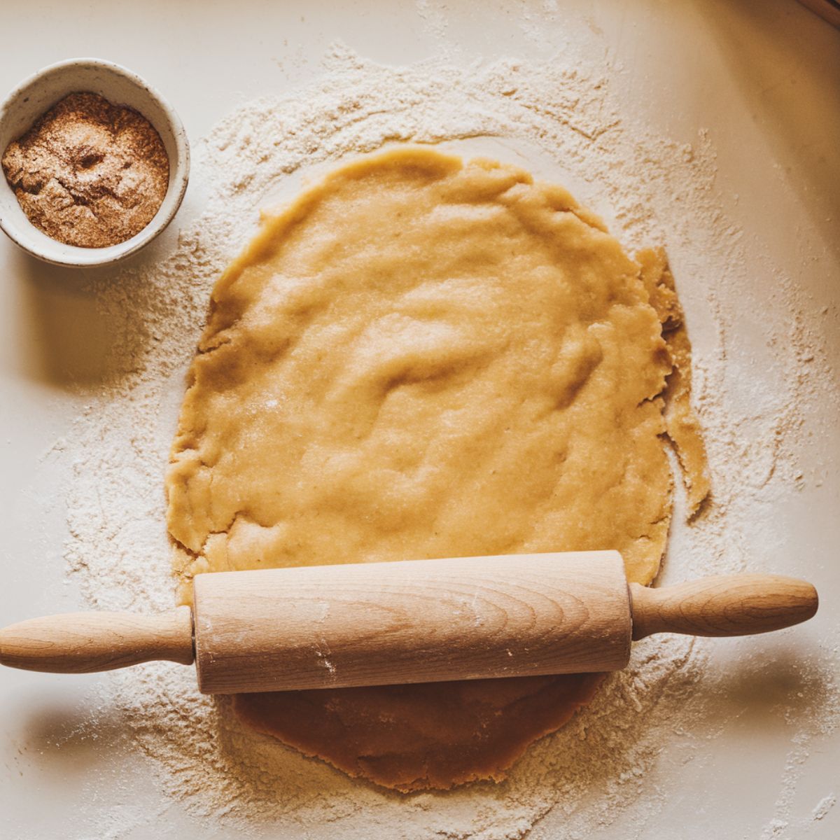 rolling pin in use of rolling out dough on a floured kitchen counter, with cinnamon sugar ready to be sprinkled.