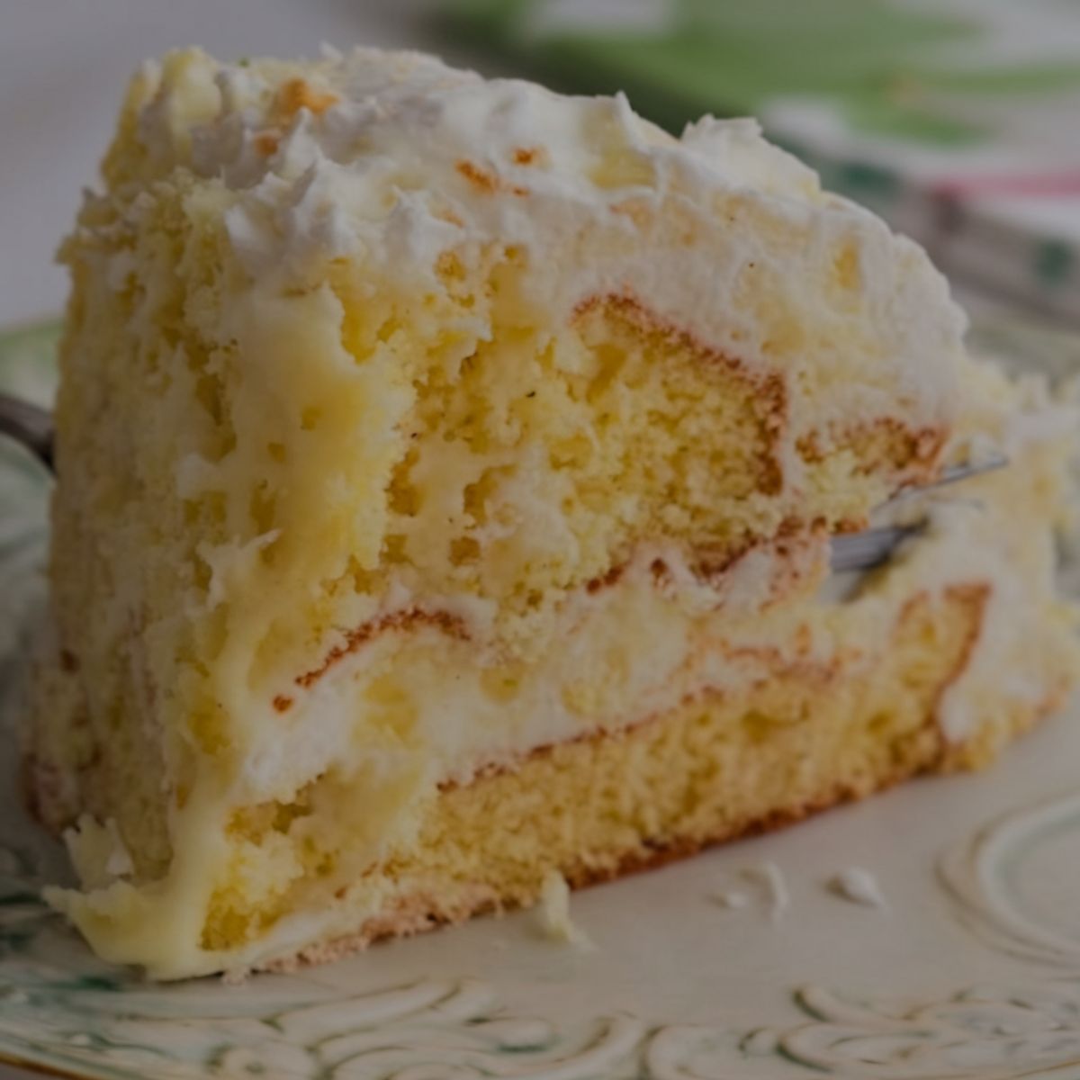 close-up of a moist slice of Pig Pickin Cake with creamy pineapple frosting on a decorative plate, showing its fluffy texture.