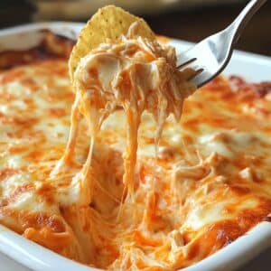 Close-up of a chip scooping hot buffalo chicken dip with stretchy, melted cheese. Rich, creamy texture with visible chicken and golden cheesy topping.