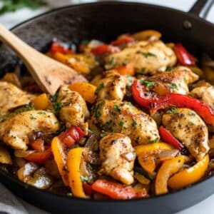 A sizzling skillet of homemade chicken with peppers and onions, cooked to golden perfection on a white kitchen counter.