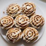 Freshly baked cinnamon roll muffins with a gooey swirl and drizzled glaze on a home kitchen counter.