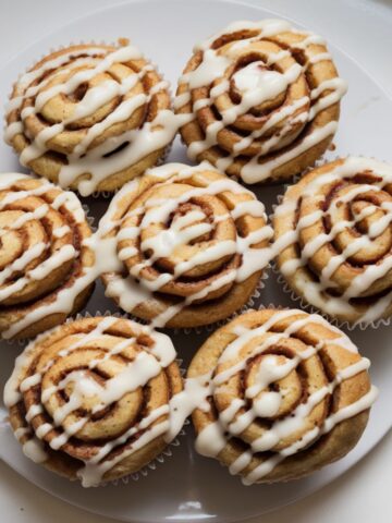 Freshly baked cinnamon roll muffins with a gooey swirl and drizzled glaze on a home kitchen counter.