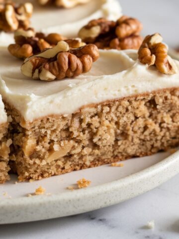 Moist gluten free banana cake topped with creamy frosting and crunchy walnuts, served on a rustic plate."