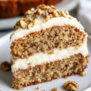 A moist gluten free banana cake slice with cream cheese frosting and chopped walnuts on top. The slightly crumbly texture and casual frosting swirls create a warm, homemade feel.