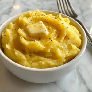 mashed potato squash with creamy interior and melting butter on a white small bowl over white counter.