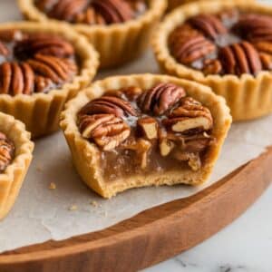 Freshly baked pecan tassies cooling on a wooden tray on a white marble kitchen counter, showcasing their golden crusts and rich pecan filling.