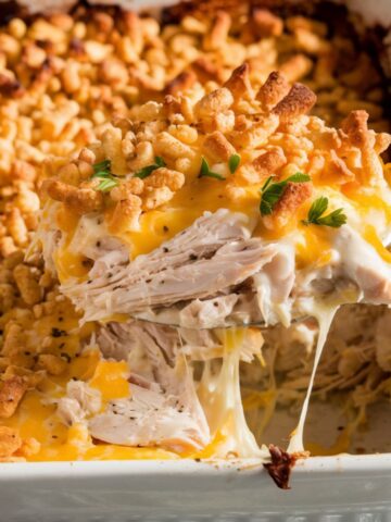 Golden, cheesy Ritz cracker chicken casserole with a crispy topping, served fresh from the oven. A spoon lifts a gooey, creamy portion with melted cheese stretching.