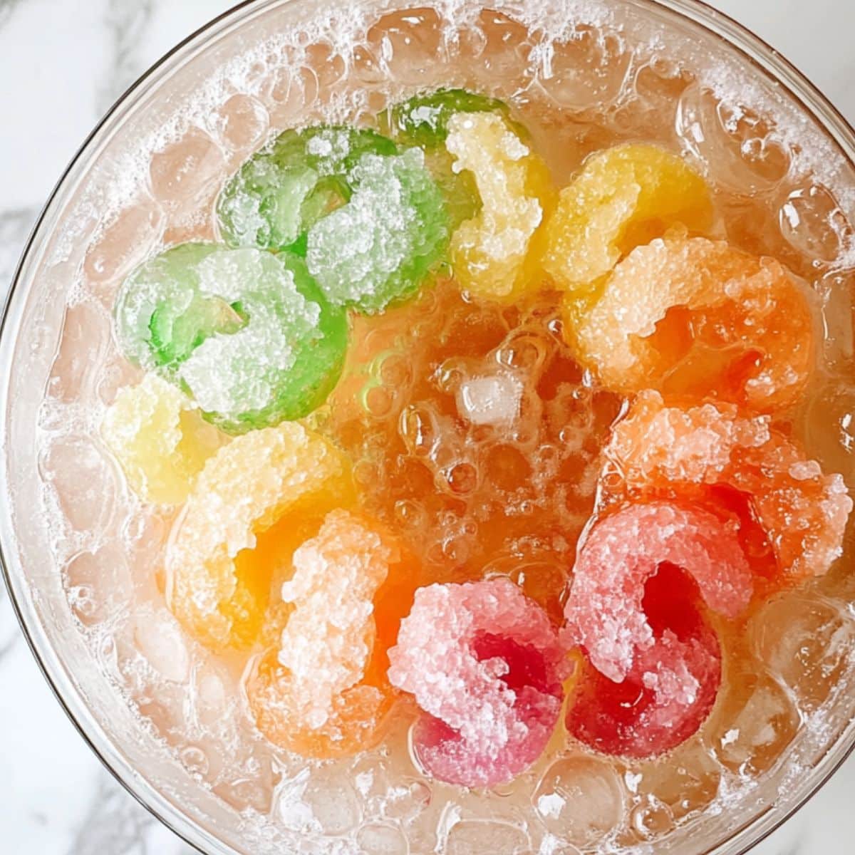 Punch bowl with ice ring in the center, sherbet scoops (green, pink, orange, yellow) being added, fizz beginning to form. Some soda already poured.