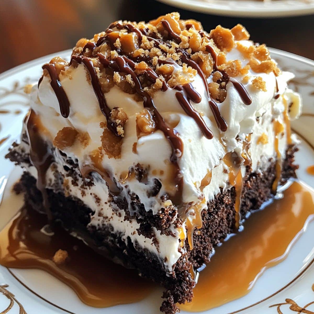 Slice of better than sex cake topped with whipped cream, caramel, chocolate drizzle, and toffee bits, served on a dessert plate with sauce pooling around the base.