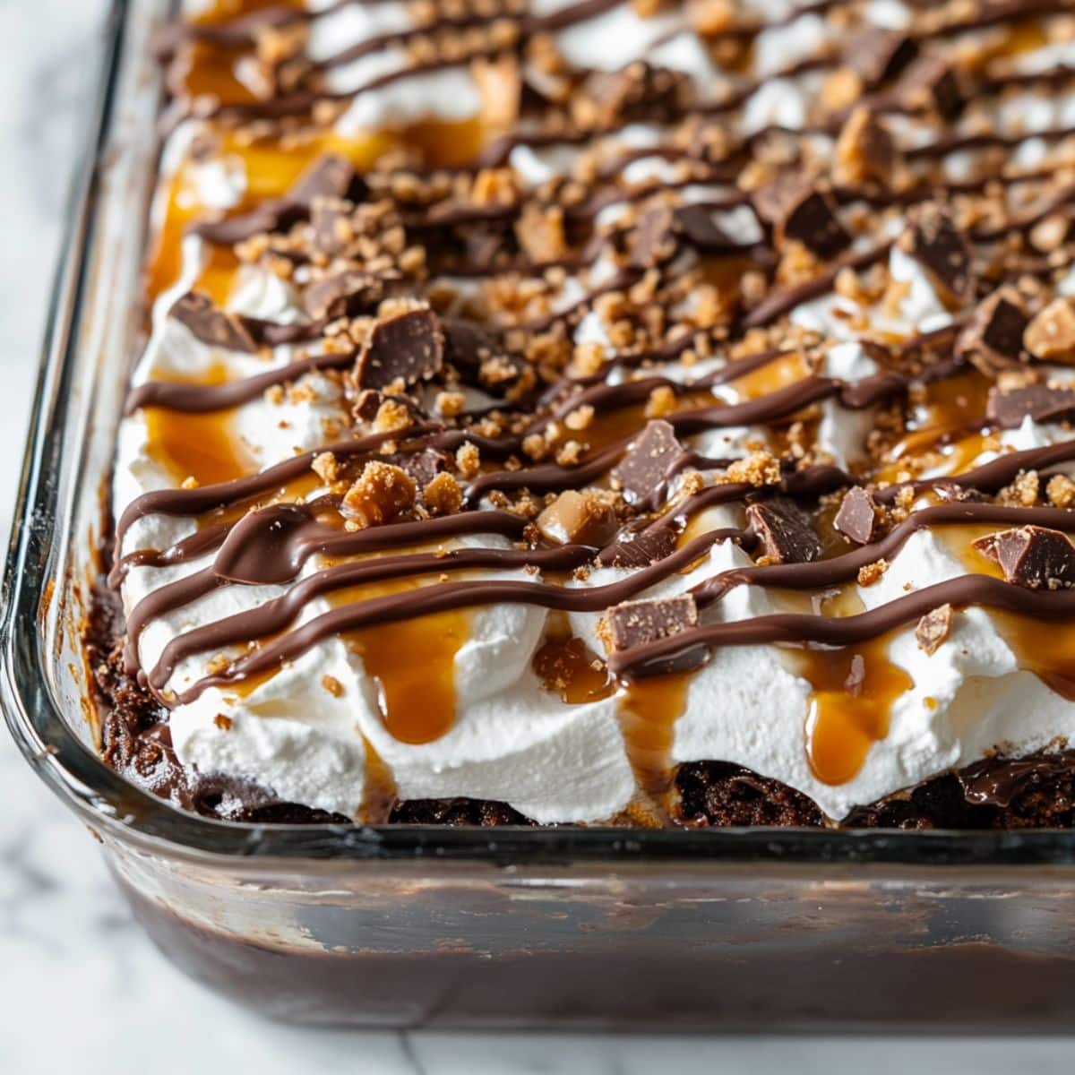 Better than sex cake in a glass dish, topped with whipped cream, caramel, chocolate drizzle, and crushed toffee candy.