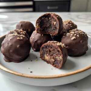 Close-up of homemade brownie truffles on a ceramic plate, one cut open to reveal rich, fudgy chocolate center.