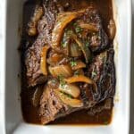 Slow cooked French onion pot roast with onions and gravy in a rustic white dish. Comforting Sunday dinner served homemade-style.