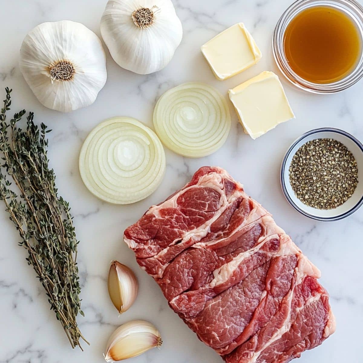 French onion pot roast ingredients inclusing chuck roast, sliced onions, French onion soup mix, garlic, thyme, butter, and beef broth arranged on a white counter, slightly cluttered.