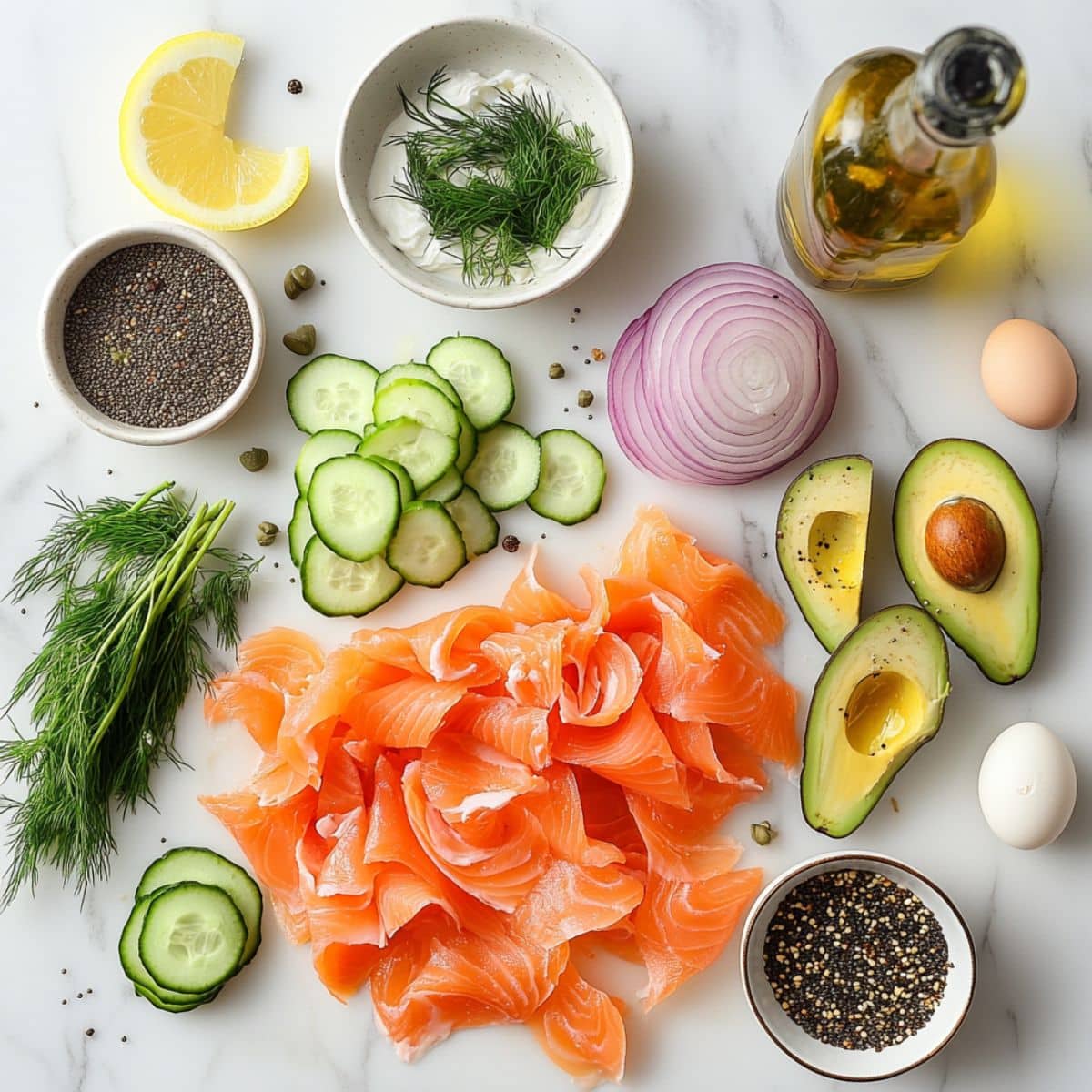 Fresh ingredients for smoked salmon breakfast including salmon slices, avocado, cucumber, lemon, cream cheese, capers, and bagels on a white marble kitchen counter.