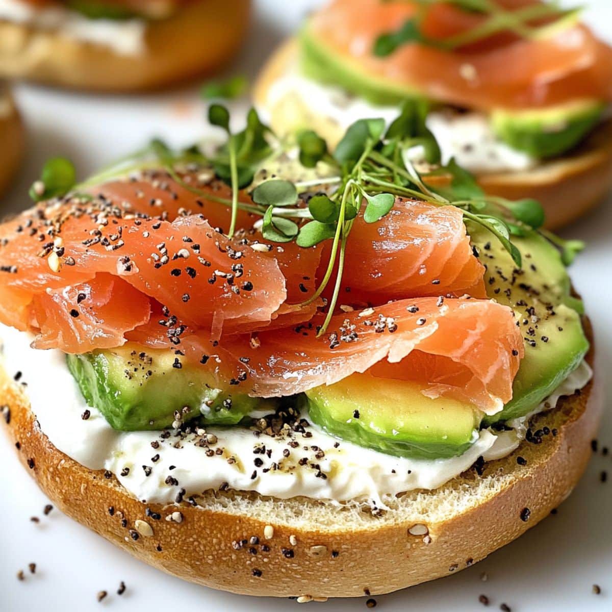Smoked salmon breakfast bagel with cream cheese, avocado slices, and fresh toppings on a white marble kitchen counter. A homemade smoked salmon breakfast perfect for weekends.